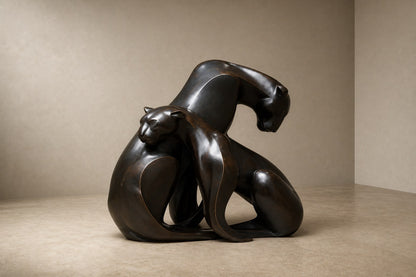 Near-black patinated bronze sculpture Pedregal, two big-cat figures entwined as a single mass, shown on a travertine display plinth.