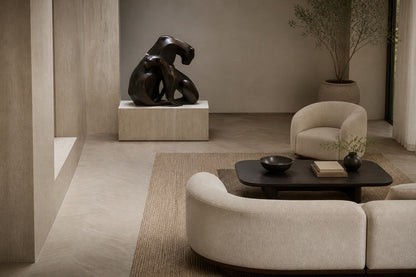 Near-black patinated bronze sculpture Pedregal, two big-cat figures entwined as a single mass, shown on a travertine display plinth.