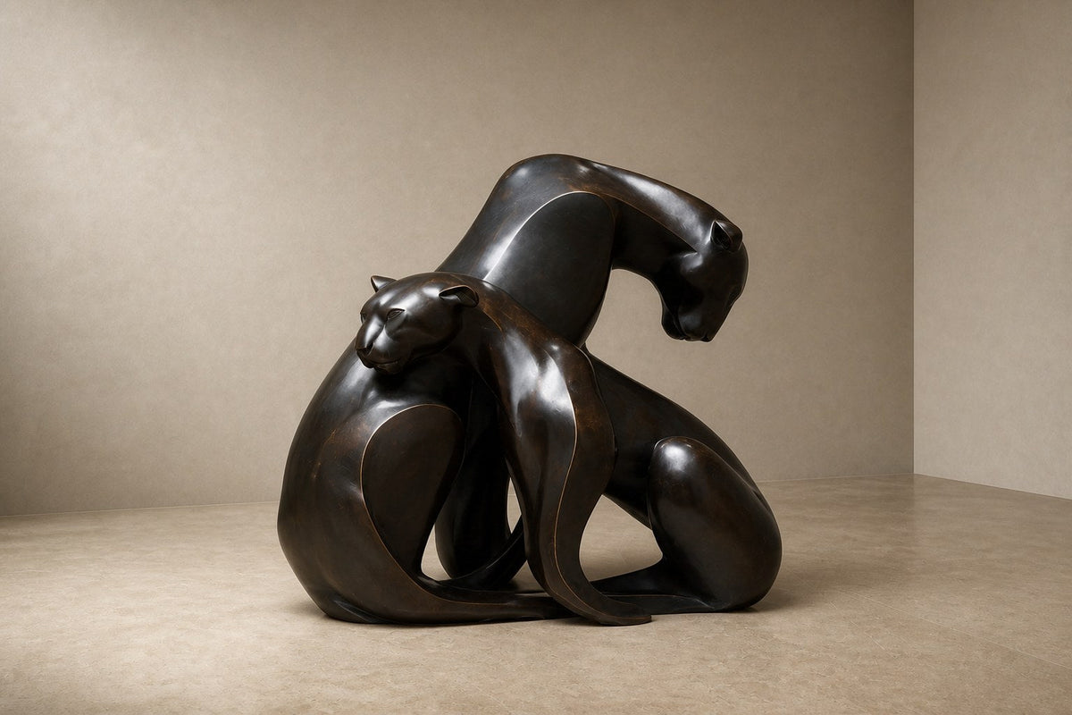 Near-black patinated bronze sculpture Pedregal, two big-cat figures entwined as a single mass, shown on a travertine display plinth.