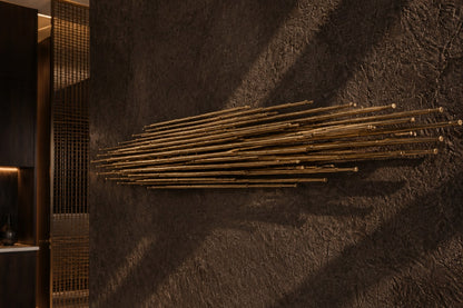 Horizontal sheaf of long polished brass rods tapering to points at both ends.