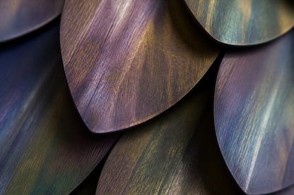 Rust orange and umber bronze wall sculpture Corteza, cast bark-textured plates shingled across a long rail, on a plaster wall.
