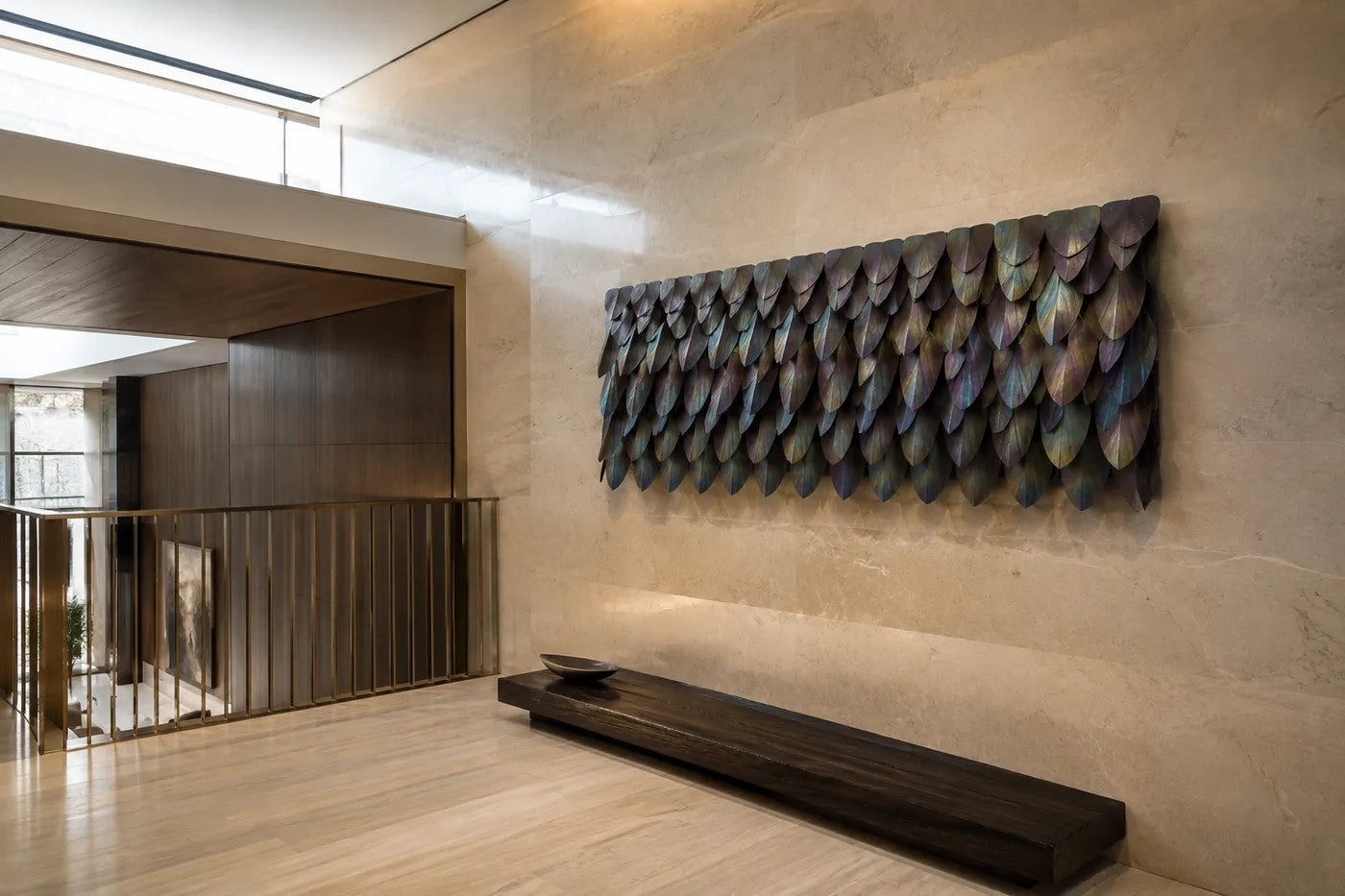 Rust orange and umber bronze wall sculpture Corteza, cast bark-textured plates shingled across a long rail, on a plaster wall.