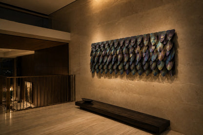 Rust orange and umber bronze wall sculpture Corteza, cast bark-textured plates shingled across a long rail, on a plaster wall.