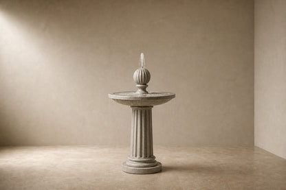 Pale limestone pedestal fountain Rivella Ø65, pale grey-white with soft veining, on a pale stone floor.
