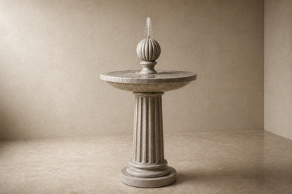 Pale limestone pedestal fountain Rivella Ø65, pale grey-white with soft veining, on a pale stone floor.
