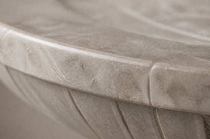 Pale limestone pedestal fountain Rivella Ø65, pale grey-white with soft veining, on a pale stone floor.