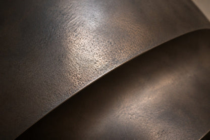 Large ovoid bronze sculpture cut open to reveal a polished interior, standing on a stone floor.