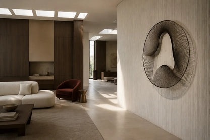 Smoke grey bronze wall sculpture Nebulosa, fine wire woven across a circular rim around a drifting void, on a plaster wall.