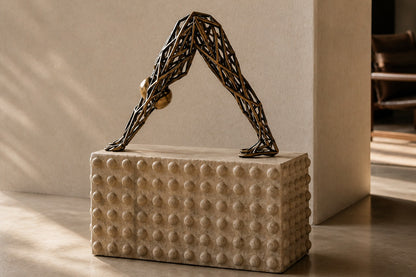Bronze strut-cage sculpture Sbalzo forming an inverted arch, gilt and blackened, on a beaded travertine block.