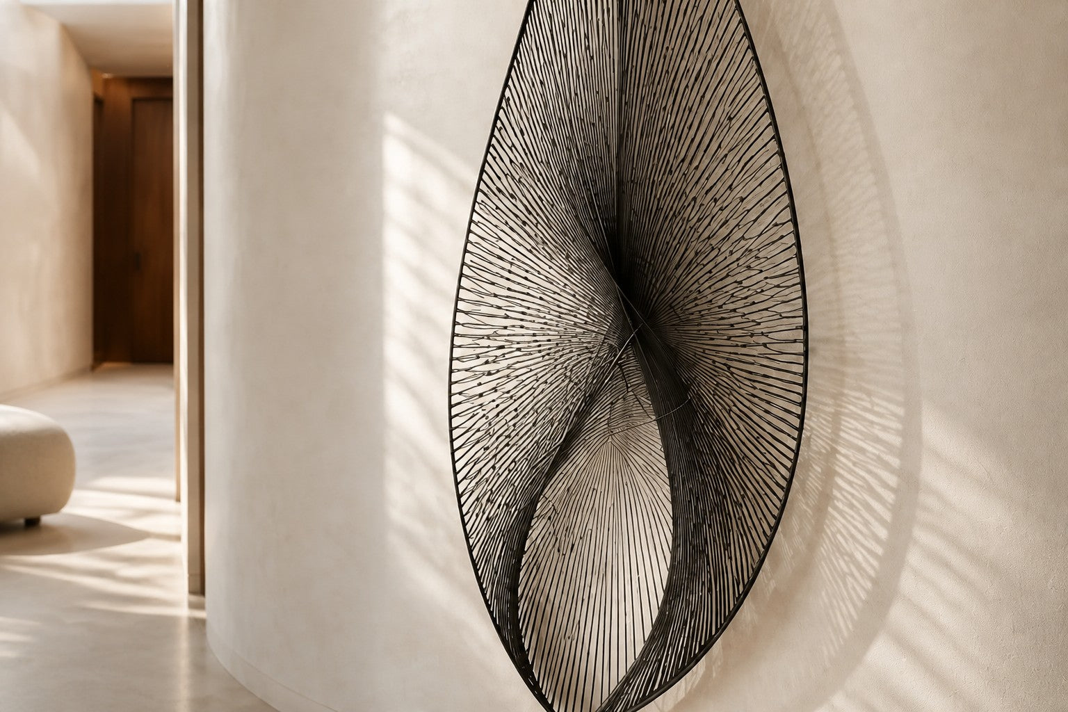 Satin steel steel wall sculpture Punta, a tapered leaf blade on a concealed bracket, on a plaster wall.