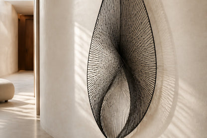 Satin steel steel wall sculpture Punta, a tapered leaf blade on a concealed bracket, on a plaster wall.