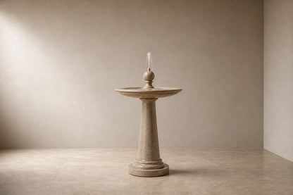 Pale limestone pedestal fountain Sorgia Ø65, warm cream with fine speckle, on a pale stone floor.