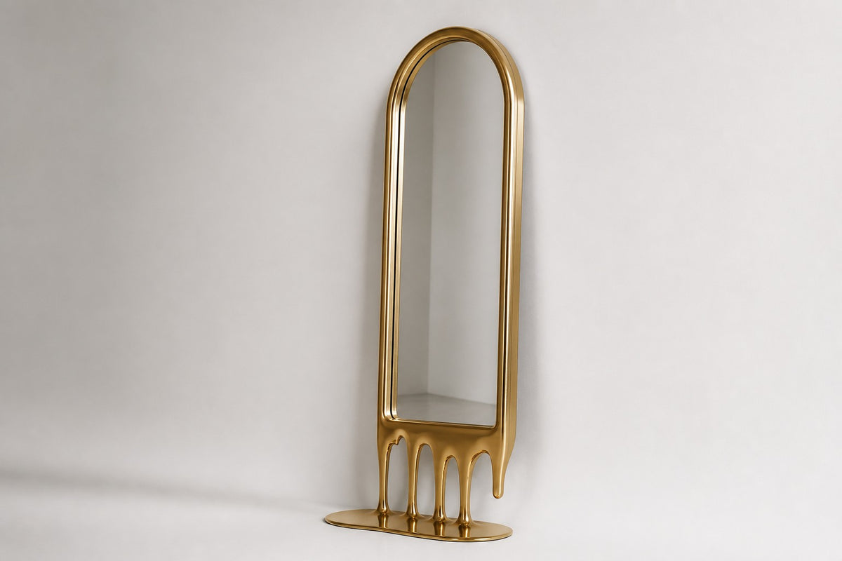 Stilla — tall arched floor mirror whose champagne brass frame melts into drips, studio side angle showing its depth