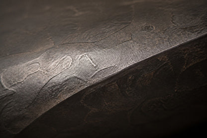 Charcoal-bronze stone fire table Suiran 220, charcoal with a warm bronze cast, on a pale stone floor.