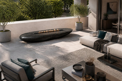 Charcoal-bronze stone fire table Suiran 220, charcoal with a warm bronze cast, on a pale stone floor.