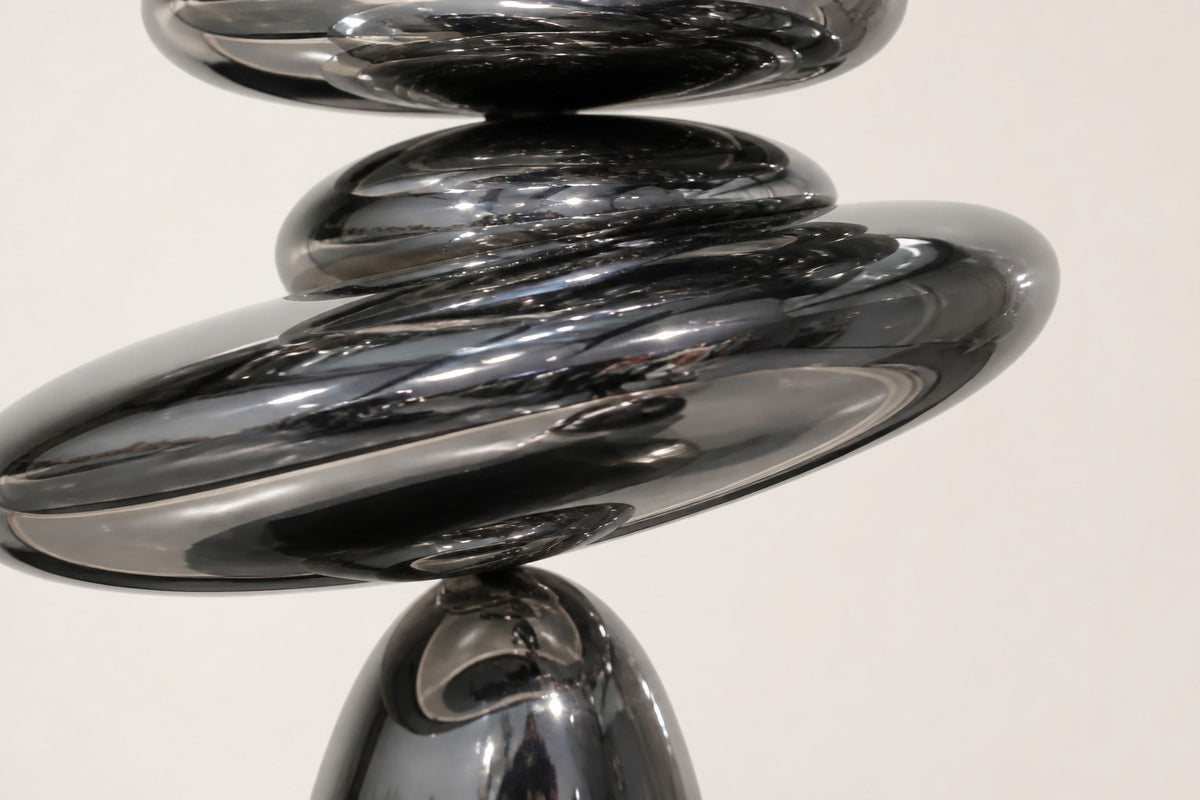 Suiseki — mirror chrome stacked pebble sculpture on a black base, close detail of the surface and edge