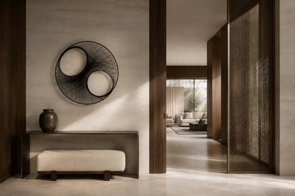 Charcoal steel wall sculpture Gemelos, two matched voids drawn in fine wire across one rim, on a plaster wall.