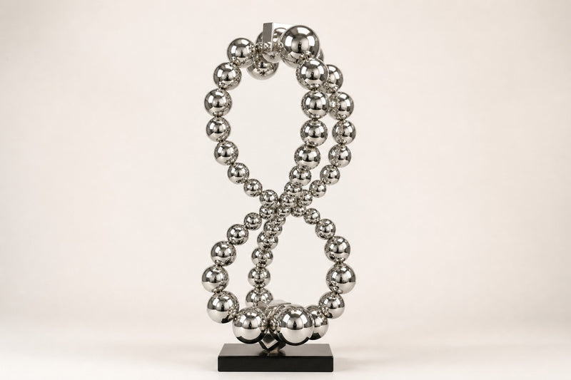 Thuraya — mirror chrome beaded figure-eight sculpture on a black base, studio front view