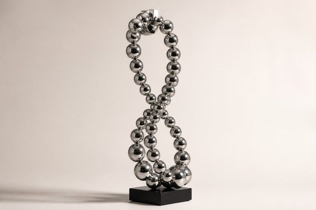 Thuraya — mirror chrome beaded figure-eight sculpture on a black base, studio side angle showing its depth