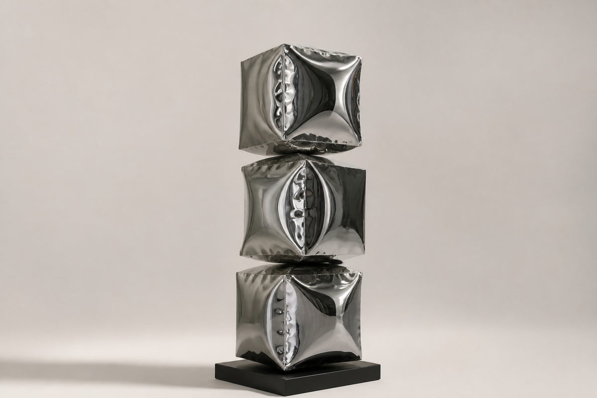 Tsumiki — 90 cm three stacked mirror-chrome inflated cubes on a black base, three-quarter studio view showing its profile