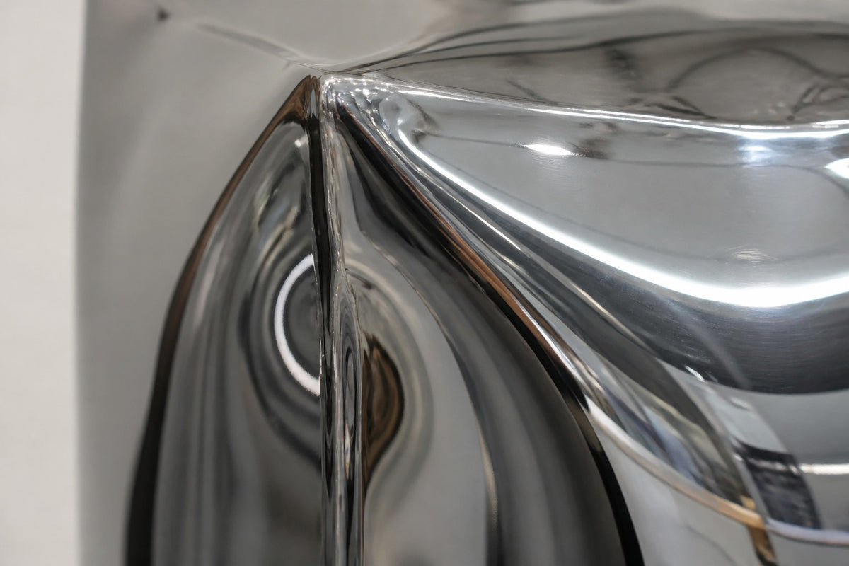 Tsumiki — 90 cm three stacked mirror-chrome inflated cubes on a black base, close studio detail of the surface and material