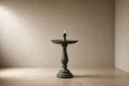Stone pedestal fountain Verdara Ø65, verdigris green over grey, on a pale stone floor.