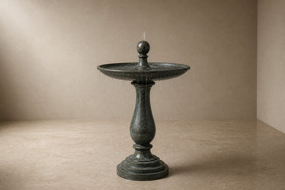 Stone pedestal fountain Verdara Ø65, verdigris green over grey, on a pale stone floor.