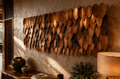 Wide panel of overlapping leaf forms in graded brown tones, leaning against a plaster wall.
