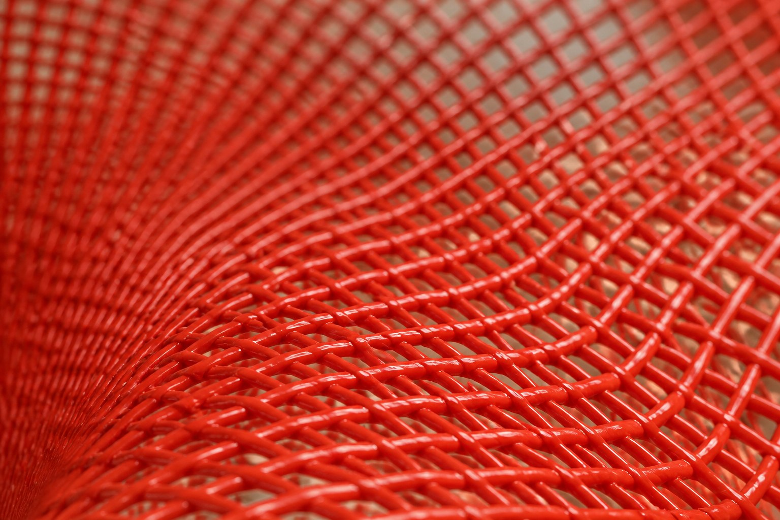 Coral red woven wire sculpture Zaurak, two full lobes drawn together through a narrow twist at the centre.