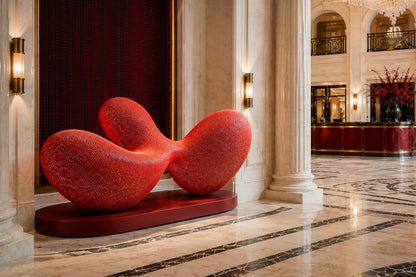 Coral red woven wire sculpture Zaurak, two full lobes drawn together through a narrow twist at the centre.