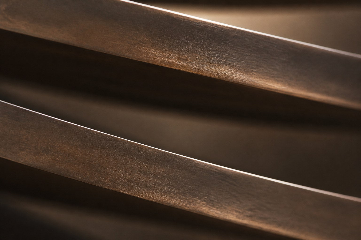 Stacked curved bronze blades tapering downward to a point, mounted on a plaster wall.